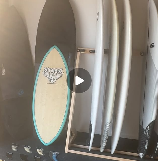 Surfboard rack at Lineup Supply holding several second hand boards, with a Strapper board and a row of fins alongside
